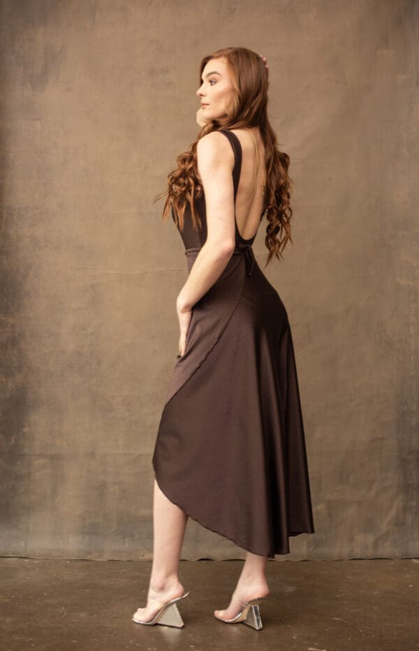 A woman in a brown dress standing next to a wall.